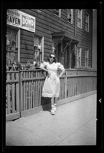 A woman in a dress stands in front of a fence