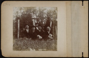 Portrait of men sitting in grass by a fence