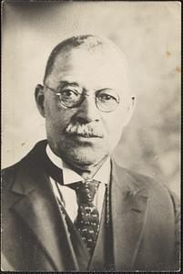 A man with a moustache, wearing glasses and a suit