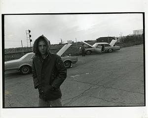 Boy in a parka and two cars next to train tracks