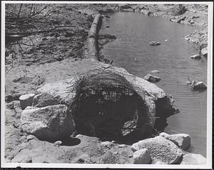 Pipe laying next to water on downstream side of dam, cement showing
