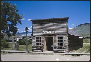 Building with "Cheap Cash Store" sign in hilly landscape, Nevada City, Montana