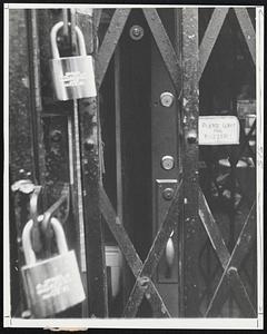 Five locks and an iron gate protect this curio shop in a New York City neighborhood where merchants and residents alike have felt the sting of crime. Even when the store is open, a customer must wait for the owner to unlock the door. The small lock at the extreme top of the picture controls the burglar alarm.