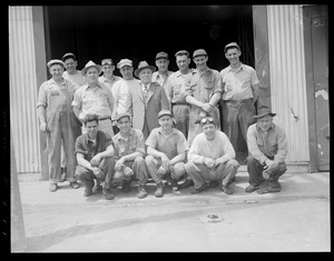Workingmen pose in front of workplace