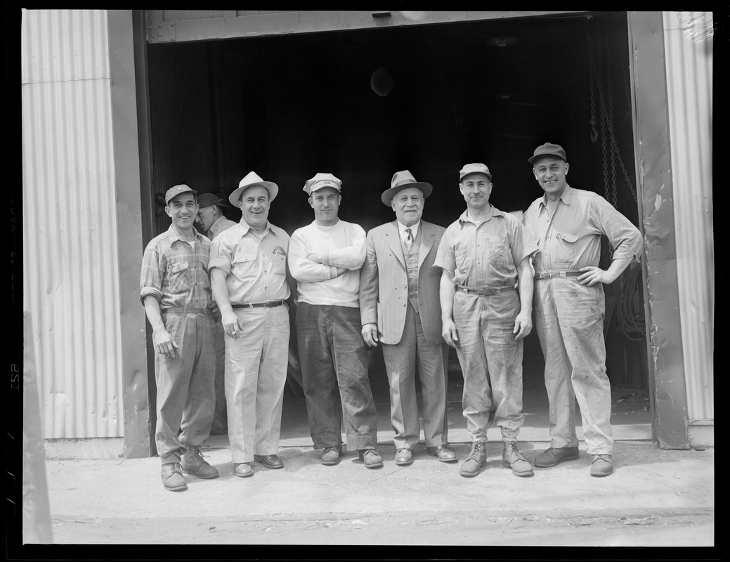 Workingmen pose in front of workplace