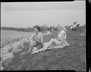 Women sit on grass next to water