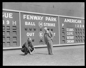 Two men inspect the grounds near left field scoreboard in Fenway
