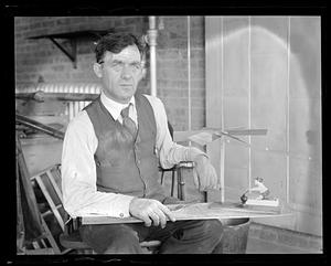 Unidentified man, seated, holding a board with a rowing figurine