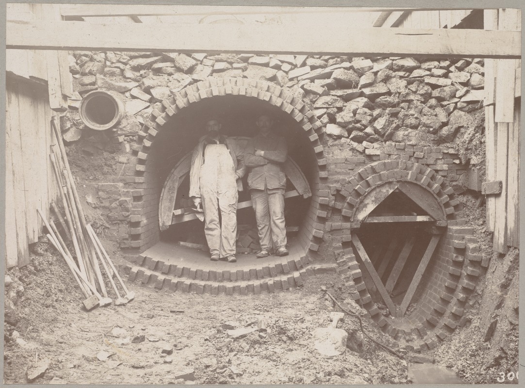 Men standing in opening of unfinished sewer