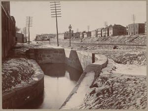Water running through stone canal by railroad tracks