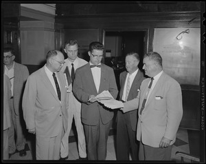 Five men standing. Man in center holds a folio of documents