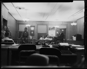 View from the desk, looking at seven men in the room