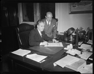 John E. Kerrigan, acting Mayor of Boston, sitting at desk signing Jerry Colonna's City of Boston award with man