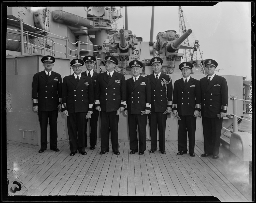 Group of men posing for picture on ship deck, in front of military weapons