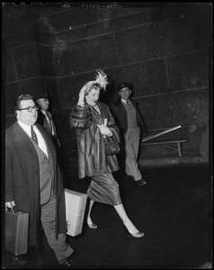 Christine Jorgenson walking with a man carrying bags, with two other men in the background