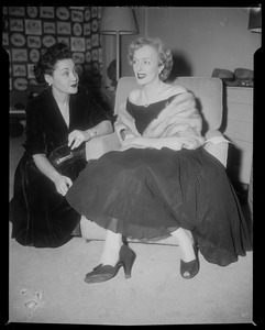 Christine Jorgenson sitting in chair, talking with another woman