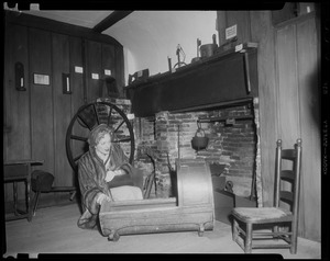 Christine Jorgenson inside Paul Revere's house, kneeling beside a rocking cradle