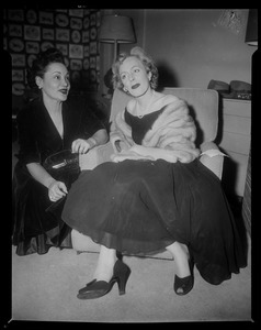 Christine Jorgenson sitting in chair, talking with another woman