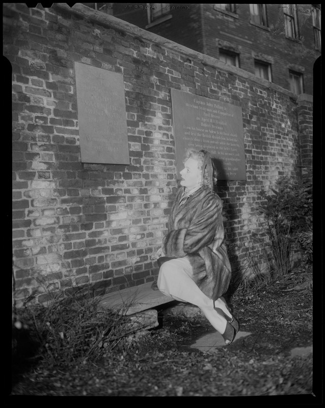 Christine Jorgenson sitting on bench in Copps Hill Burying Ground, looking at Louise Waterbury Montague plaque