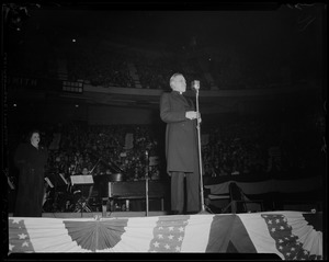 Man at microphone on stage, with Kate Smith in the background