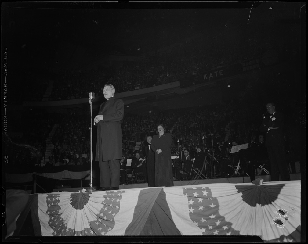 Man at microphone on stage, with Kate Smith in the background