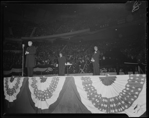 Man at microphone on stage, with Kate Smith and second man in the background