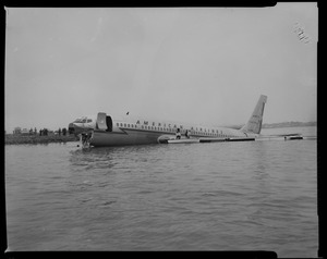 American Airlines airplane in Boston Harbor, with two men sitting on the wing and one in a boat alongside