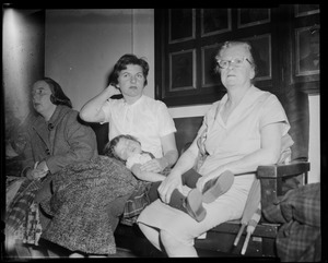 Three women seated on a bench, two with a young girl lying across their laps