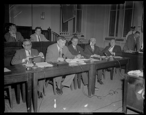 Five men sitting at table, one speaking to the room