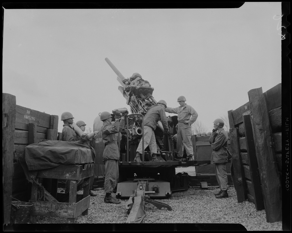 Men in military uniform loading an artillery piece and holding shells