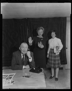 Walter Brown on phone with two women behind him, one gesturing