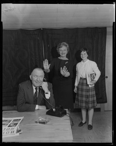 Walter Brown on phone with two women behind him, one gesturing