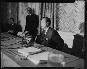 Governor George Wallace speaking while other men at a table look on