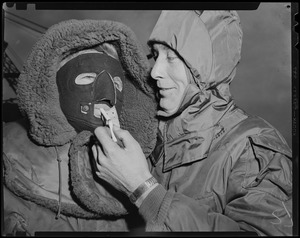 Man holding object to another's face, both in heavy coats