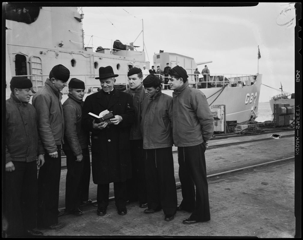 Man showing a group of sailors something from the book "The White Continent, The Story of Antarctica" by Thomas R. Henry