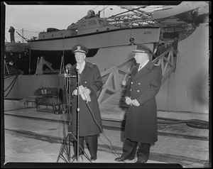 Two men speaking in front of the USS Atka
