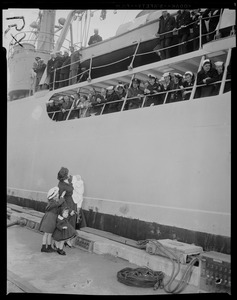 Woman and children standing on the dock looking at the crew onboard a ship