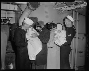 Two men and two women standing inside of a ship while holding babies