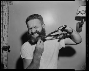 Portrait of a crew member holding a pair of scissors and trying to cut his beard