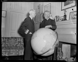 Two men standing beside a globe