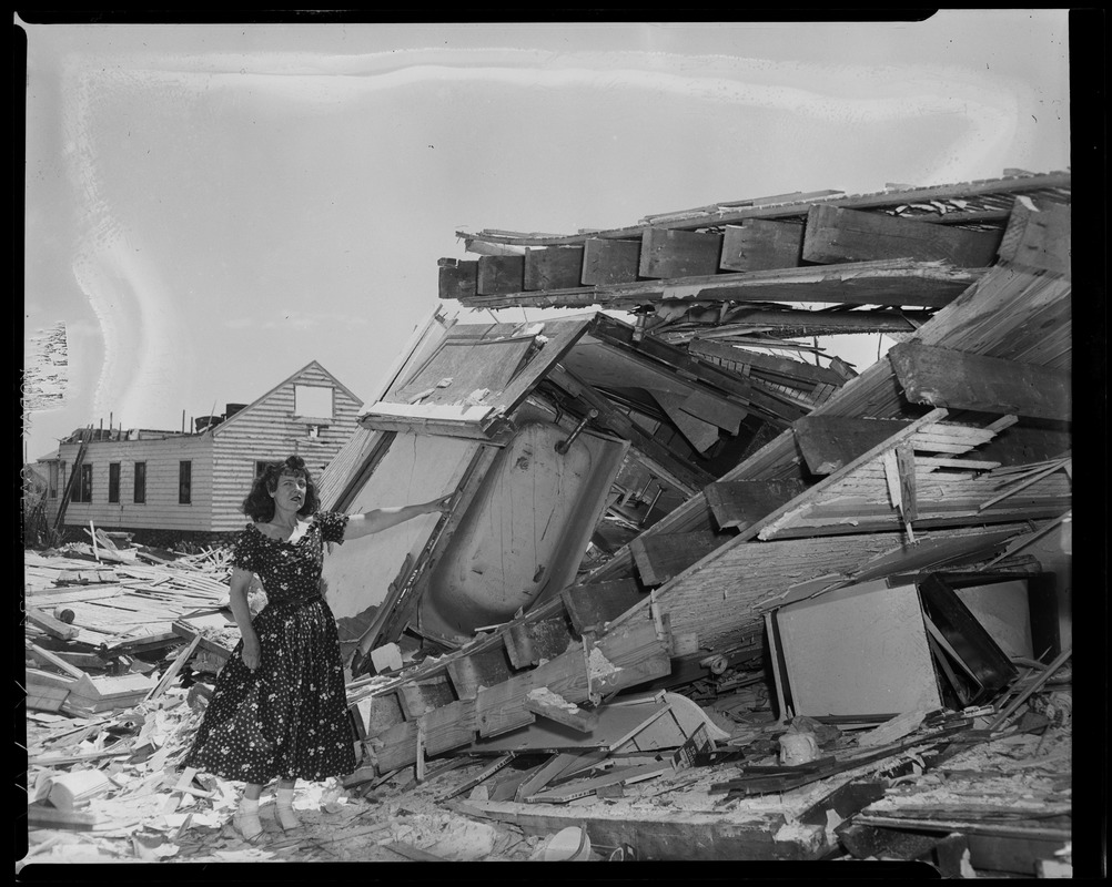 Woman in dress posing next to house destruction