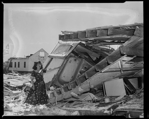 Woman in dress posing next to house destruction