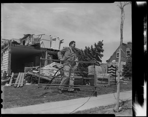 Man holding bed frame with destroyed house in background