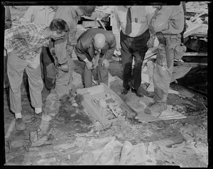 Men, some in uniform, looking at a box on the ground full of human bones