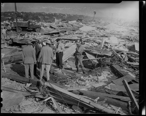 Group of men, some in uniform, standing at wreckage site with box of human bones