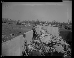 Close up of destruction, featuring beams, brick, blown off doors and walls, with people in the background