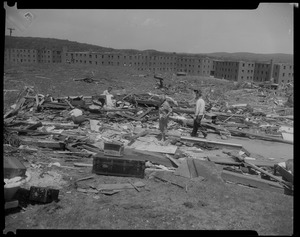 Two men and two women looking through wreckage with housing developments in the background