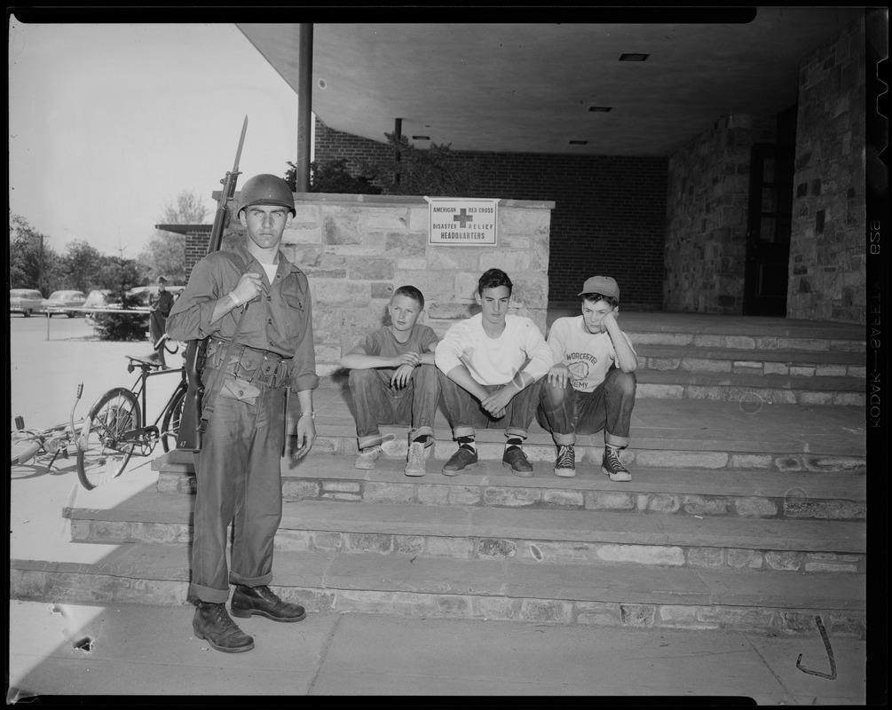 Three boys sitting on the steps of the American Red Cross Disaster Relief Headquarters with a member of the military standing alongside
