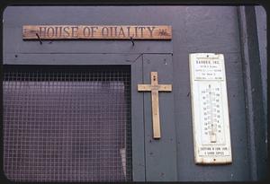 Sign reading "House of Quality" hanging on wall above cross