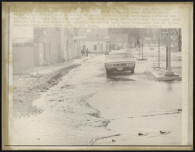 Cars try to make their way along Main street here (7/29) as mud and flood waters remain in the wake of torrential rains which dumped some 6 inches of rain in a 12 hour period. Springfield was declared a "State Disaster Area' by Governor Deane Davis. National Guardsmen were brought in to aid police in helping residents that were evacuated due to flood dangers. Many roads were washed out also.